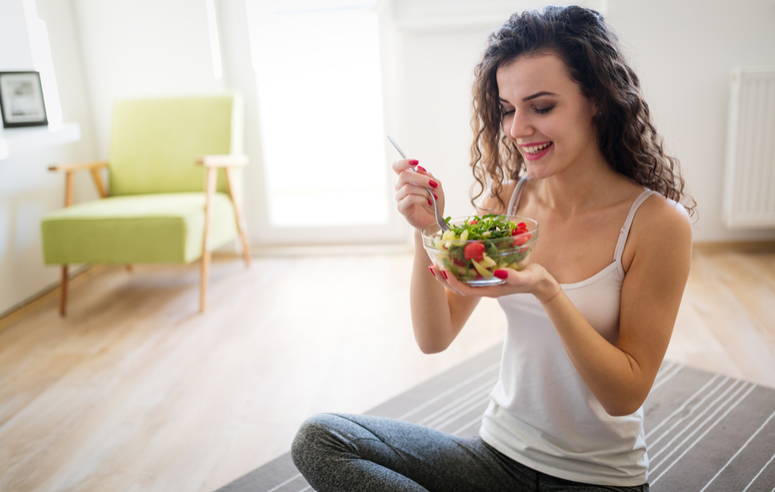Mujer-joven-sentada-en-un-sillon-comiendo-ensalada-de-vegetales